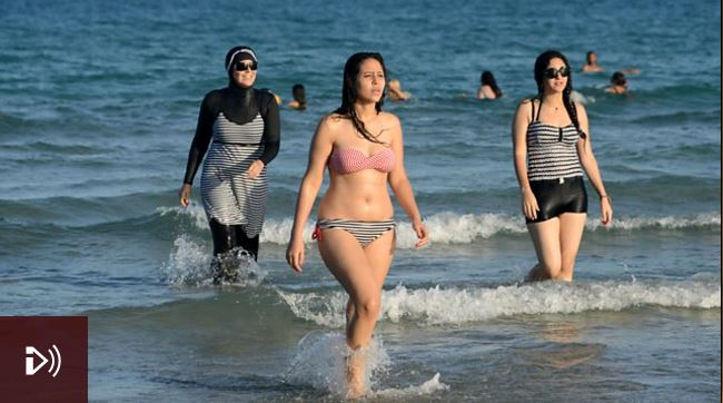 Photo: Tunisian women, one (L) wearing a ‘burkini’, at Ghar El Melh beach near Bizerte, north-east of Tunis. Credit: Fethi Belaid/AFP/Getty Images